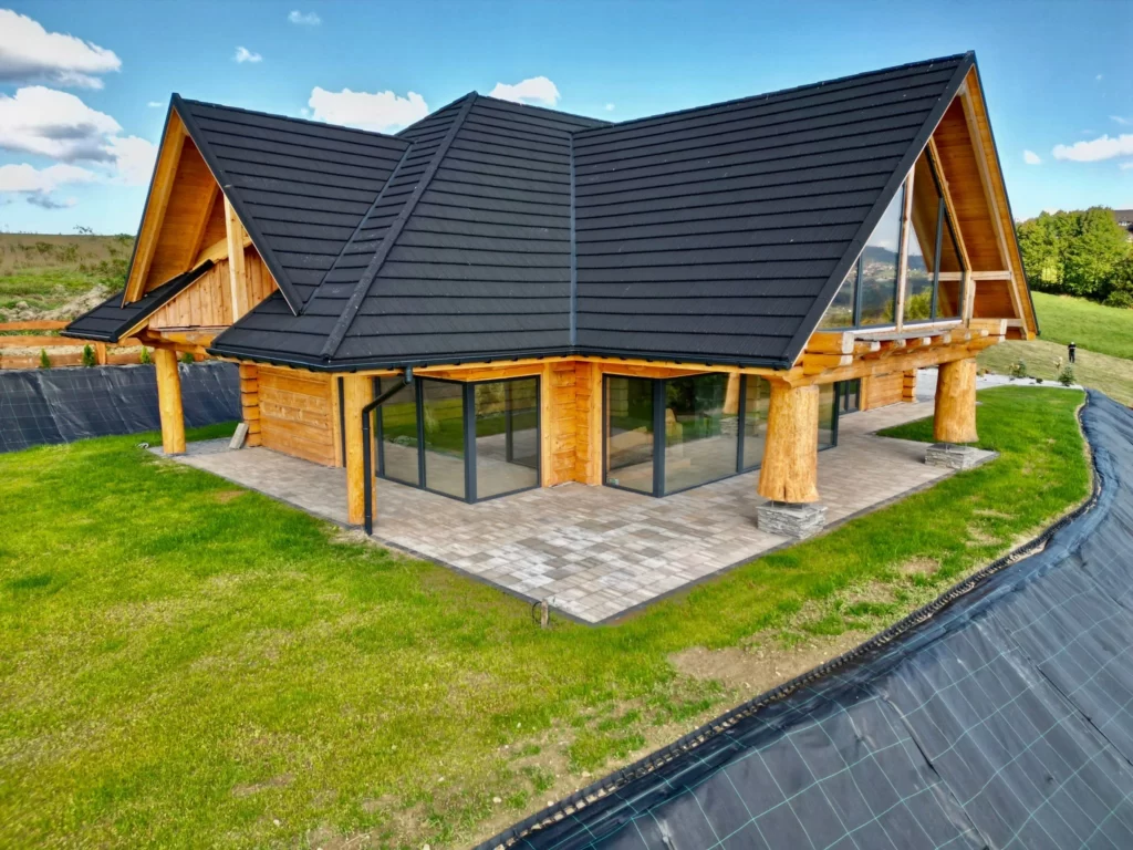 dom z bali na Złotym Groniu, duże okna tarasowe, zielona trawa w ogródku, skarpa zabezpieczona folią