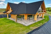 dom z bali na Złotym Groniu, duże okna tarasowe, zielona trawa w ogródku, skarpa zabezpieczona folią